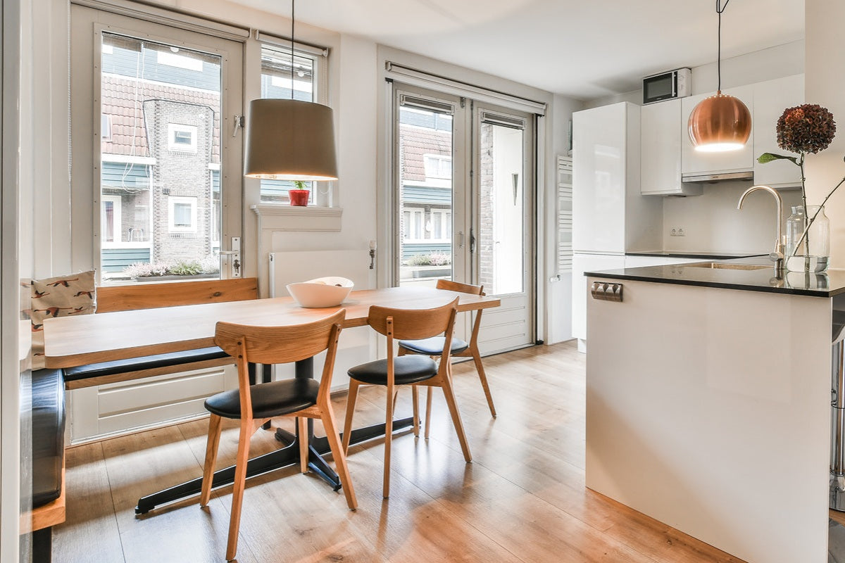 A modern open-plan dining and kitchen space with light wood flooring, a wooden dining table with black chairs, a white kitchen island, and pendant lights.